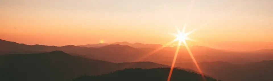 Bright yellow sunrise against an orange sky with silhouettes of the Great Smokey Mountains in the foreground.