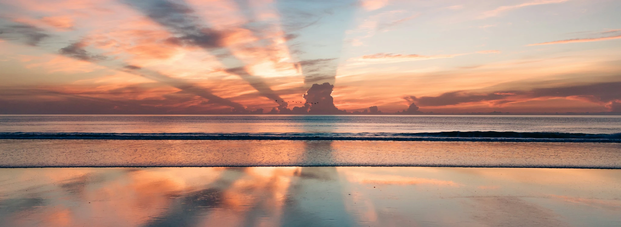 A pink and blue sunrise over the ocean mirrored on wet sand.